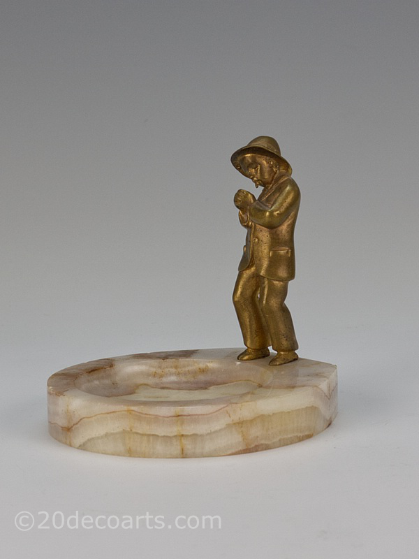  20th Century Decorative Arts |A gilded bronze figure vide-poche by Bertrand, France circa 1920s depicting a young boy in a suit lighting a cigarette mounted on a honey onyx base